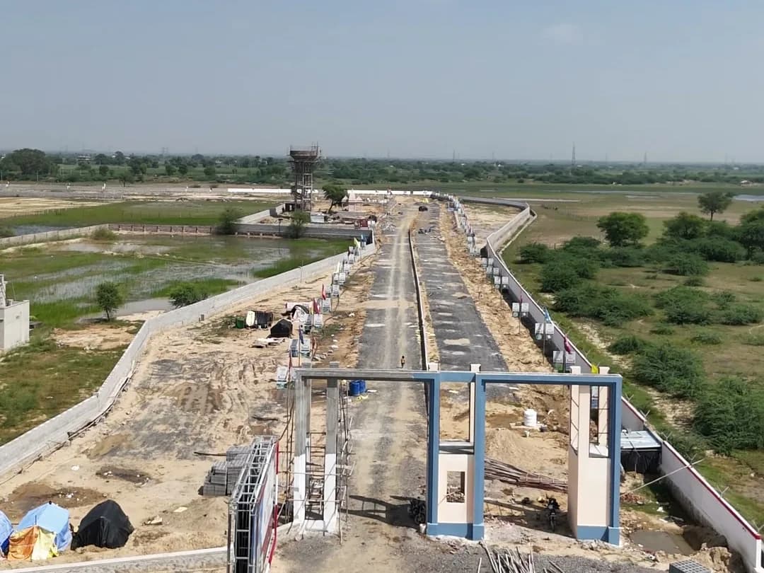 Swarn Nagri Vistar's entrance gate under construction, with the internal road and water tank behind it (drone view, 23 September 2026)