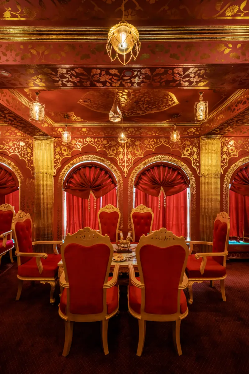 A red-and-gold dining room at Kurki Palace in Jaipur, with hand-painted walls, arched windows and carved velvet chairs