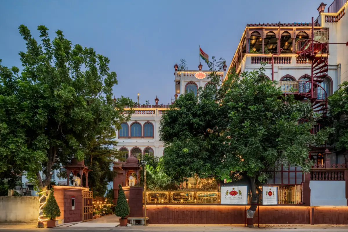 Kurki Palace in Jaipur at dusk, its facade and balconies behind trees, with the palace sign at the gate