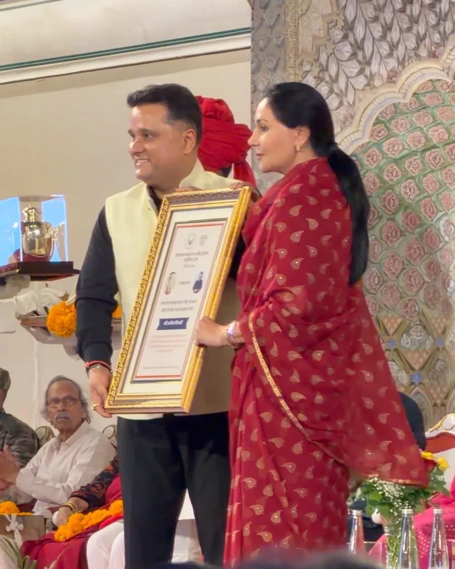 Amish Tripathi in a light yellow Nehru jacket holding a framed citation on stage