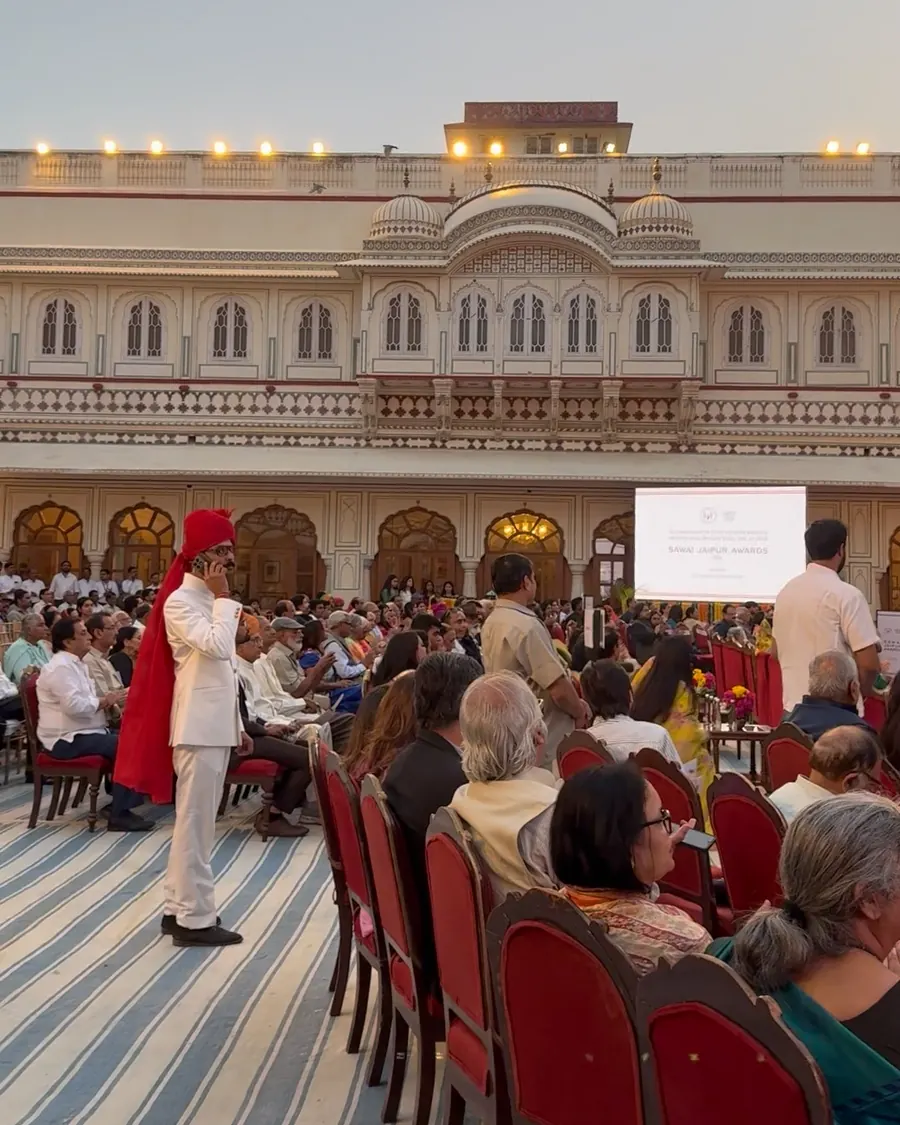 Guests seated on red chairs in the City Palace courtyard at dusk, with the palace behind them