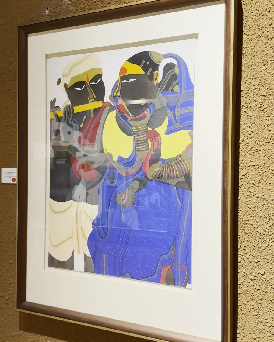 A framed work showing two figures in bold colours on an ochre gallery wall